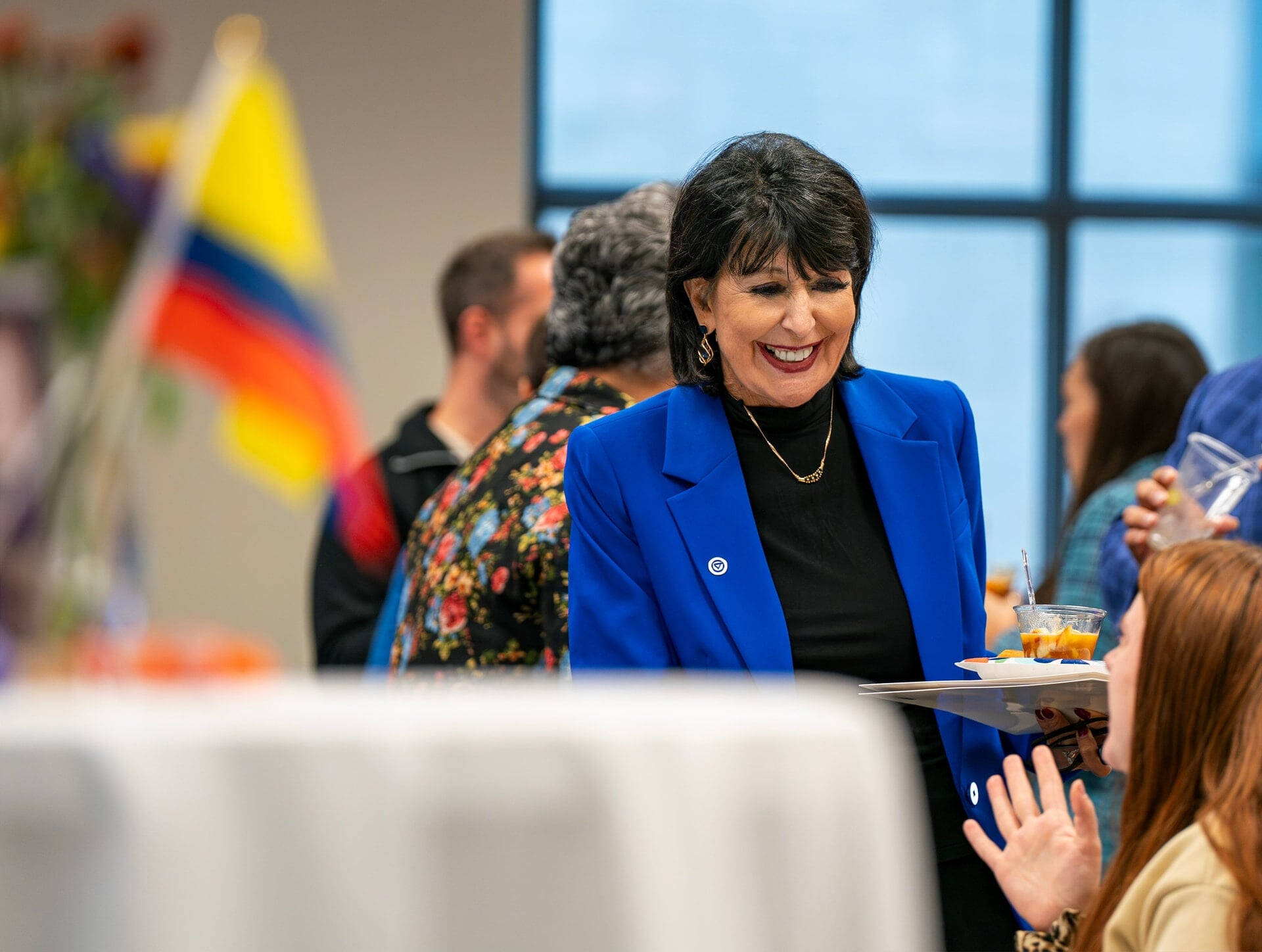 President Mantella stands in a blue blazer talking to a person seated at a table
